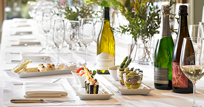 테이블 위에 음식들을 조금씩 담은 작은 그릇들이 놓여 있다. 그 옆으로 다채로운 와인과 와인 잔이 보인다.