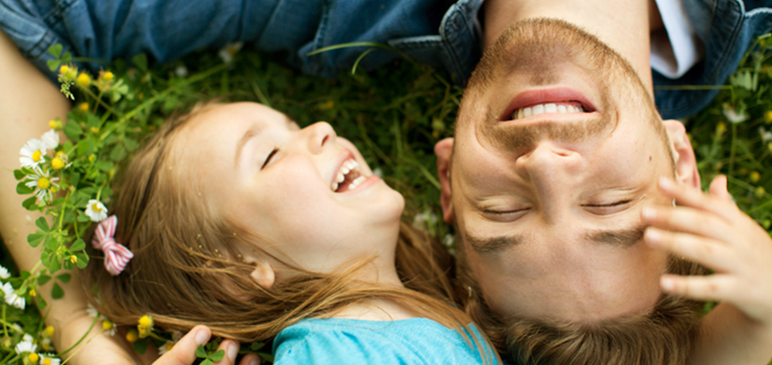 초록 잔디밭에 누운 아빠와 딸이 서로의 머리를 만지며 웃고 있다