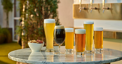 야외 테라스에 있는 테이블 위에 여러가지 맥주가 담긴 잔과 스낵이 세팅되어 있는 이미지